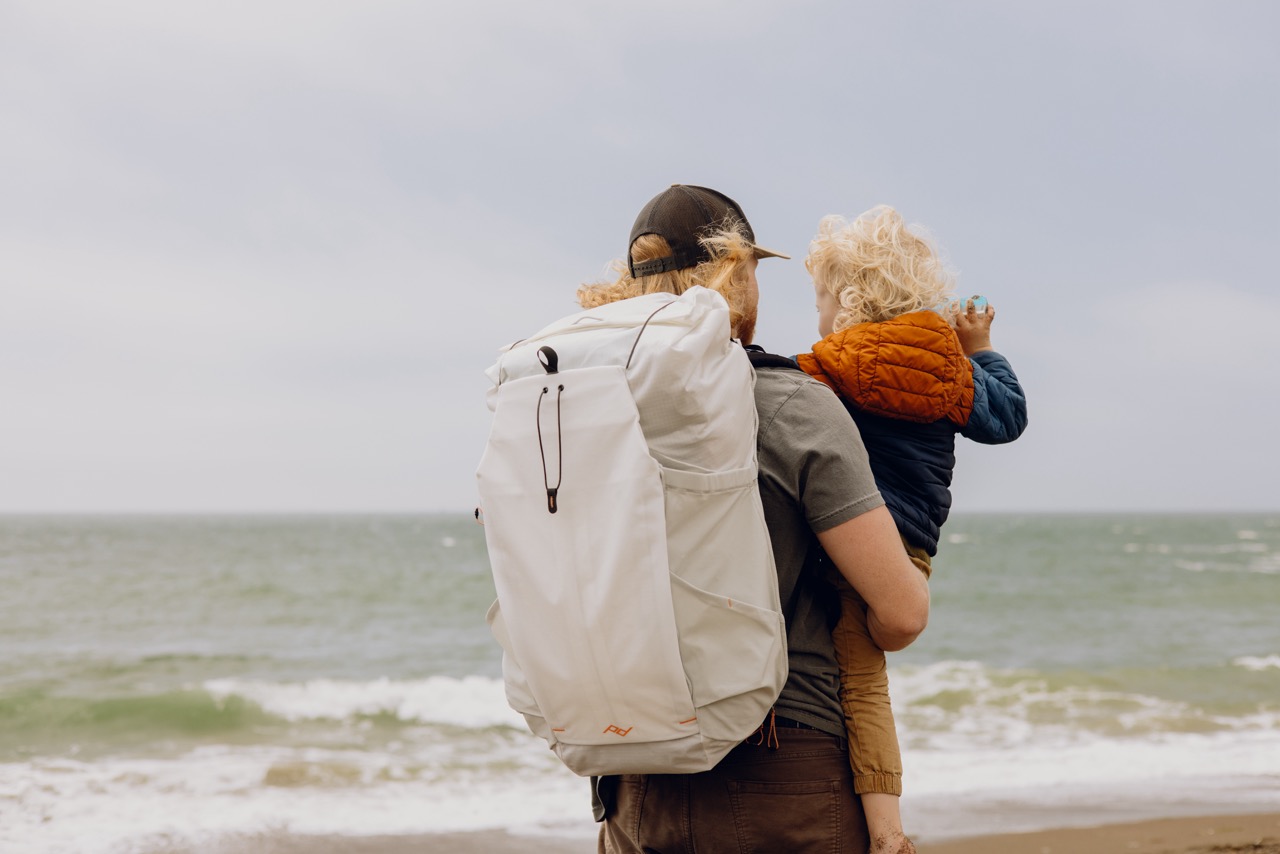 Peak Design Outdoor Backpack mit 45 Litern Fassungsvermögen in der Farbe Weiß,  Lifestyle Foto mit Rucksack auf Person vor Meeres Hintergrund